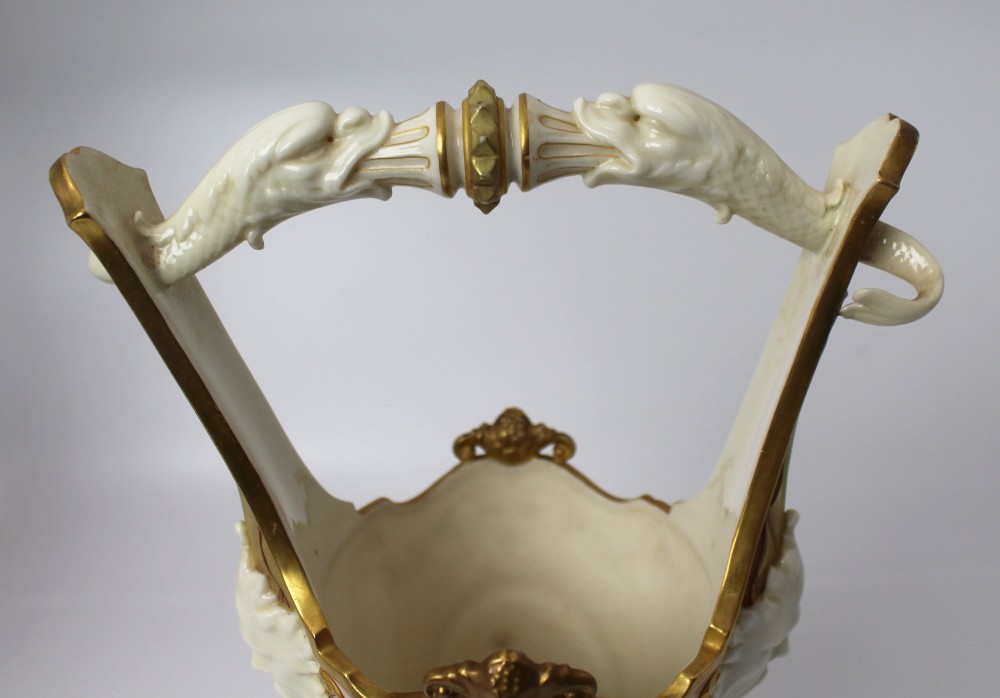 A white porcelain vase featuring a central white relief medallion of a cherub, gold gilded borders, raised side mask faces, and an overhead dolphin handle. View XIII