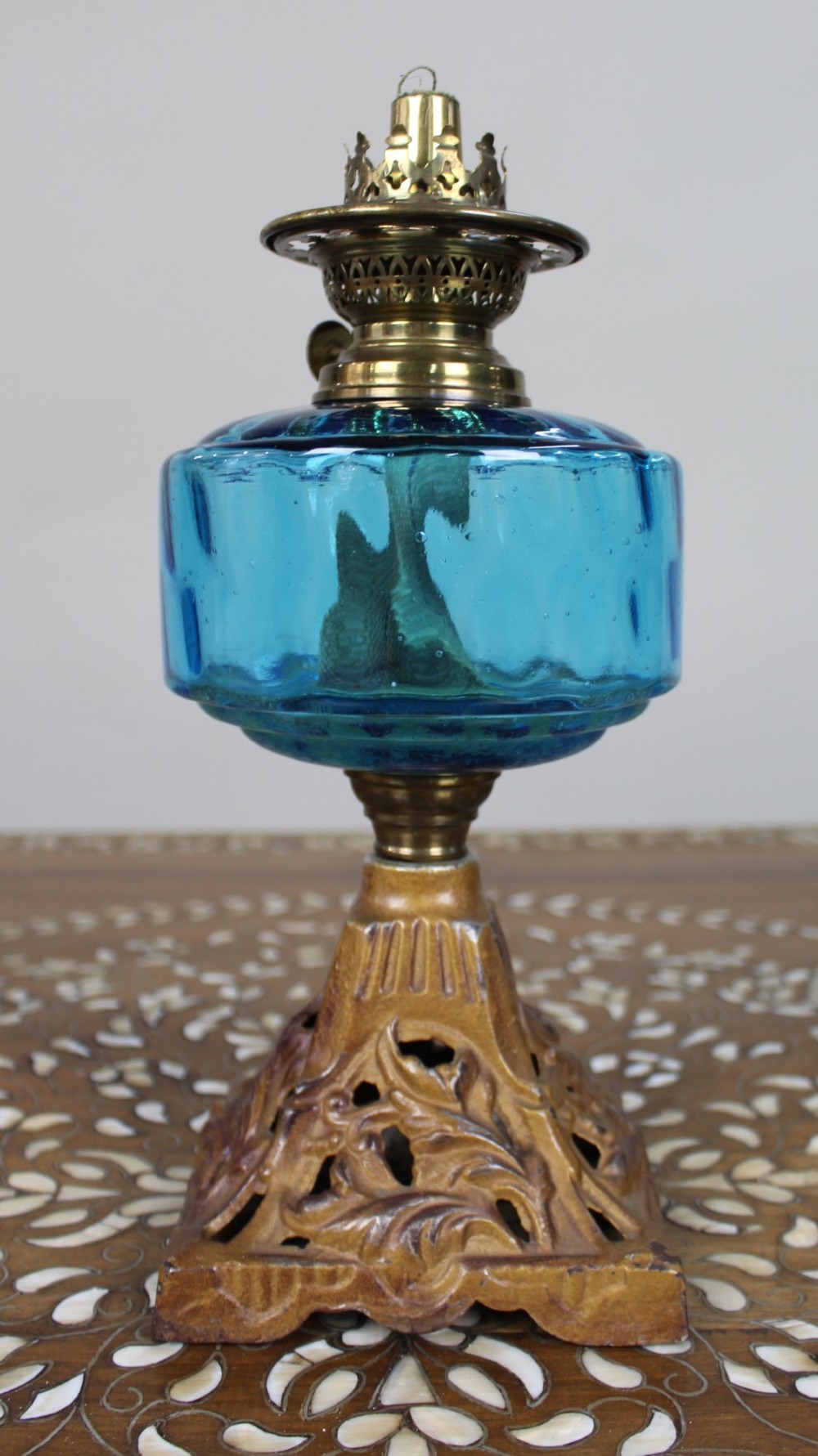 An antique Victorian oil lamp featuring a cast metal base with scrolling leaf motifs, a vibrant blue glass font, and a brass burner gallery. View II