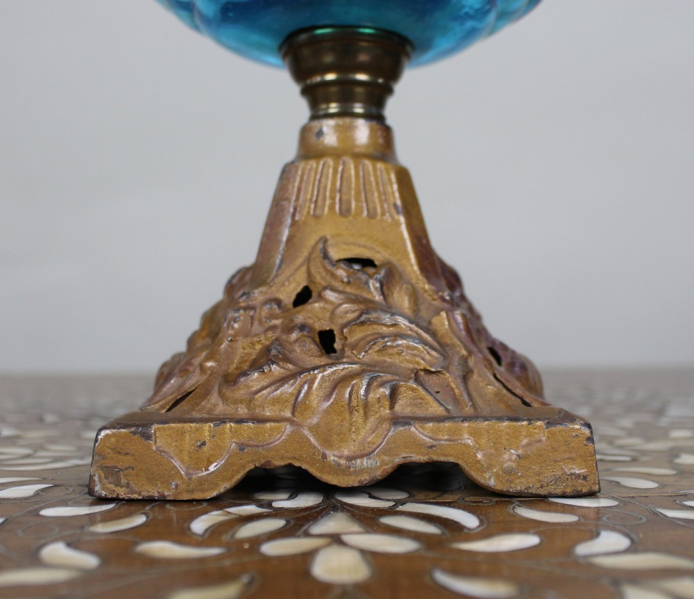 An antique Victorian oil lamp featuring a cast metal base with scrolling leaf motifs, a vibrant blue glass font, and a brass burner gallery. View III