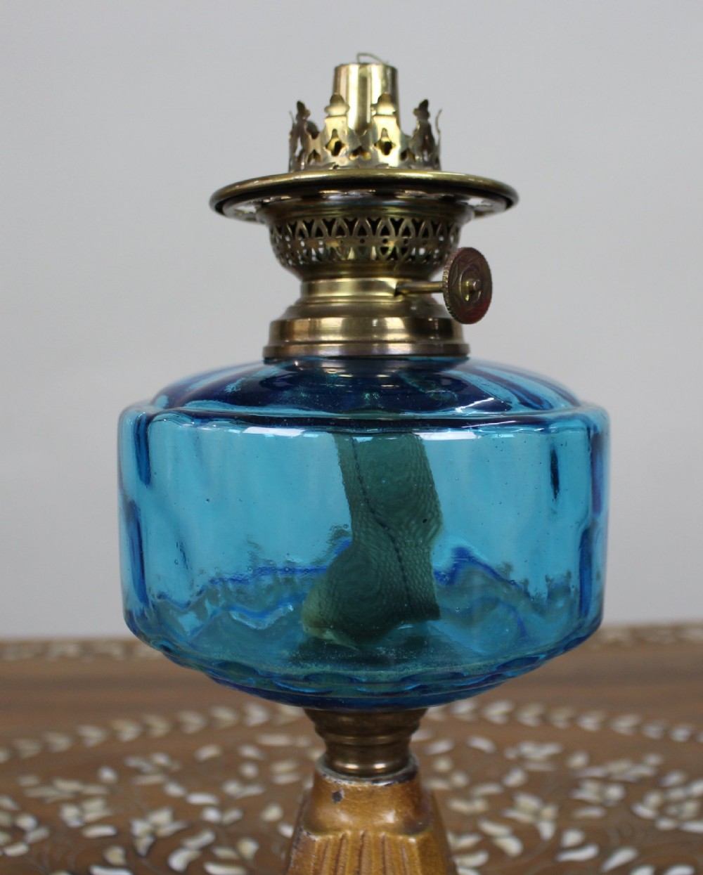 An antique Victorian oil lamp featuring a cast metal base with scrolling leaf motifs, a vibrant blue glass font, and a brass burner gallery. View IV