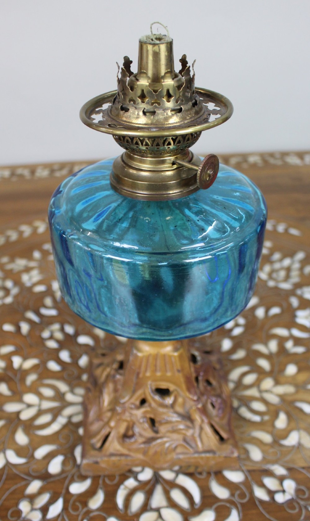 An antique Victorian oil lamp featuring a cast metal base with scrolling leaf motifs, a vibrant blue glass font, and a brass burner gallery. View V