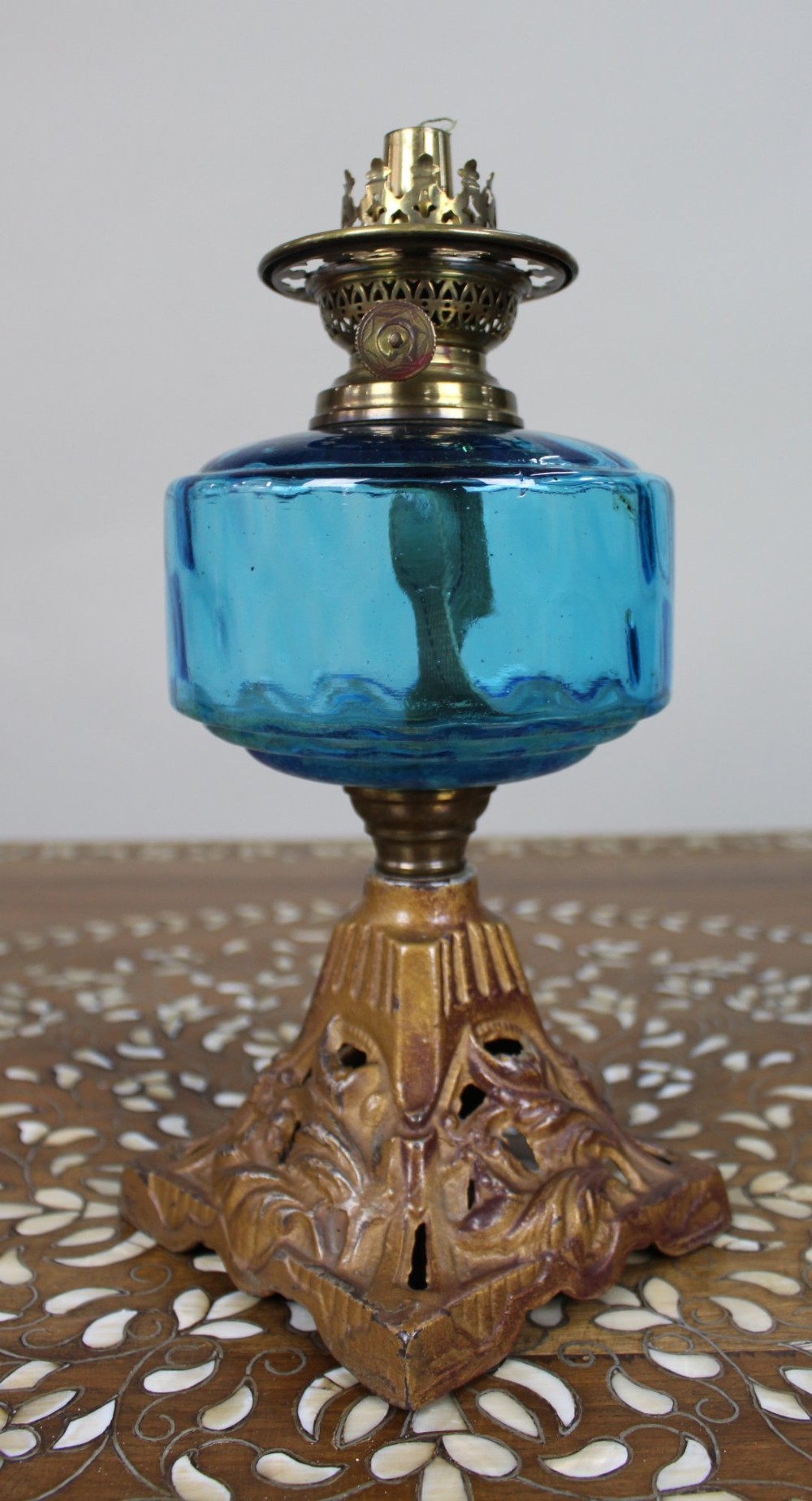 An antique Victorian oil lamp featuring a cast metal base with scrolling leaf motifs, a vibrant blue glass font, and a brass burner gallery. View VI