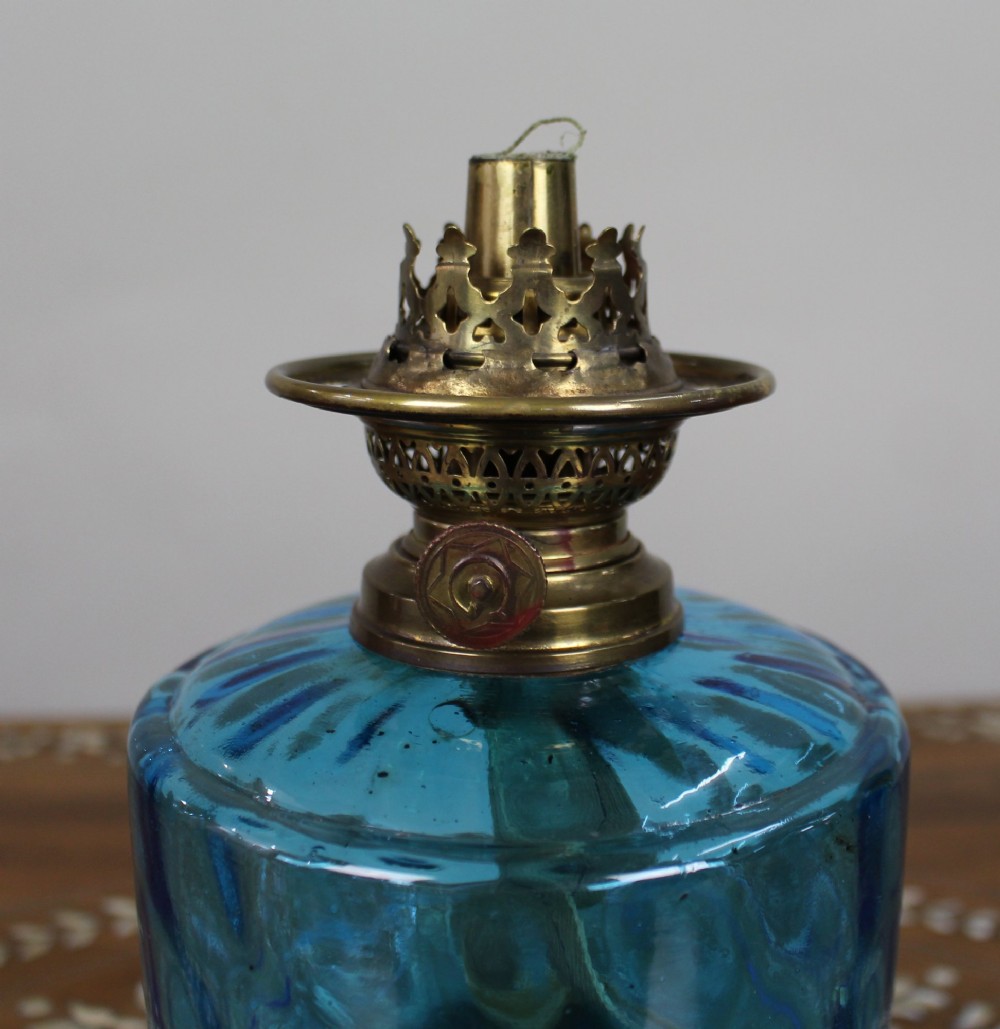 An antique Victorian oil lamp featuring a cast metal base with scrolling leaf motifs, a vibrant blue glass font, and a brass burner gallery. View VII
