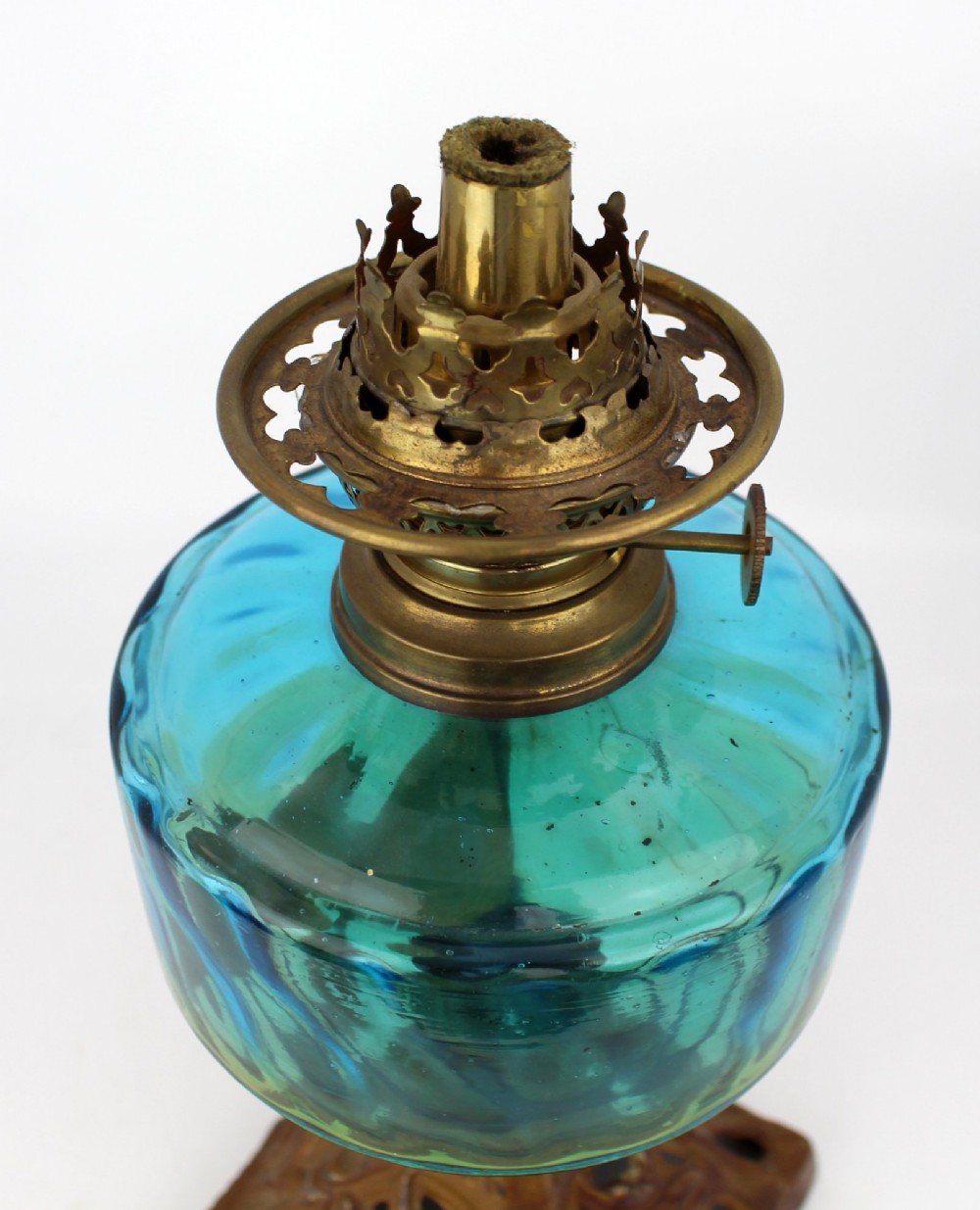 An antique Victorian oil lamp featuring a cast metal base with scrolling leaf motifs, a vibrant blue glass font, and a brass burner gallery. View X