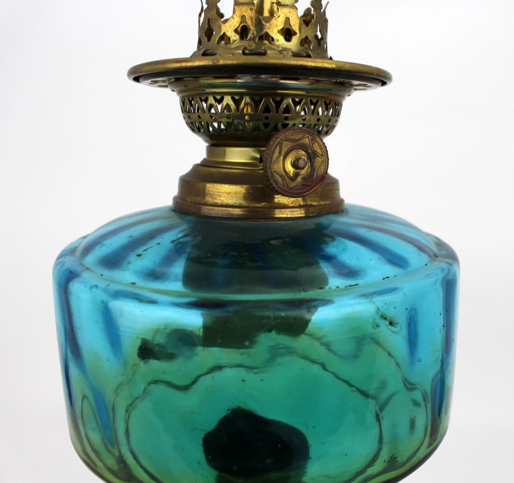 An antique Victorian oil lamp featuring a cast metal base with scrolling leaf motifs, a vibrant blue glass font, and a brass burner gallery. View XII