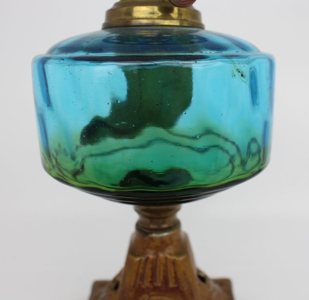 An antique Victorian oil lamp featuring a cast metal base with scrolling leaf motifs, a vibrant blue glass font, and a brass burner gallery. View XIII