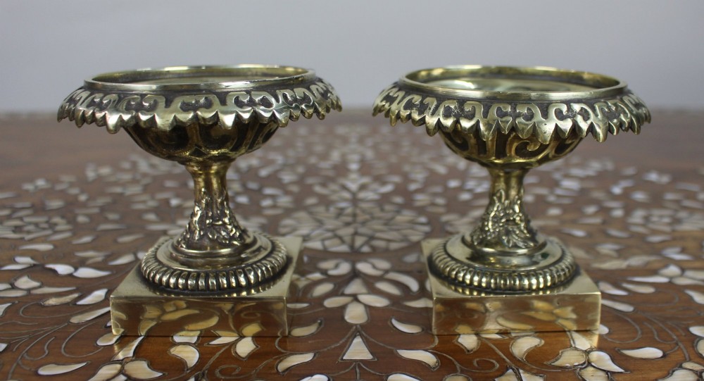 A pair of small antique bronze and brass urns featuring scalloped rims, relief scrollwork, and flared pedestals on square bases. View II