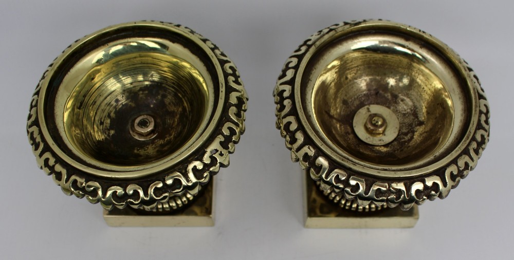 A pair of small antique bronze and brass urns featuring scalloped rims, relief scrollwork, and flared pedestals on square bases. View XII