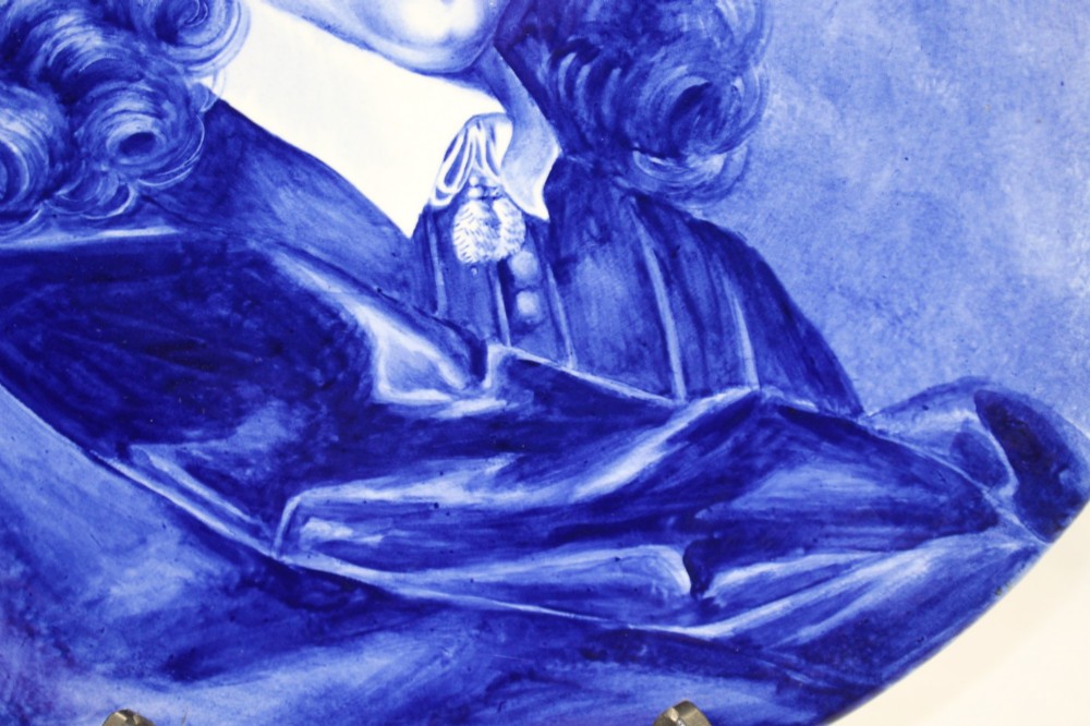 A circular glazed ceramic charger featuring a monochrome cobalt blue hand-painted portrait of a seventeenth-century man against a light blue background. View VII