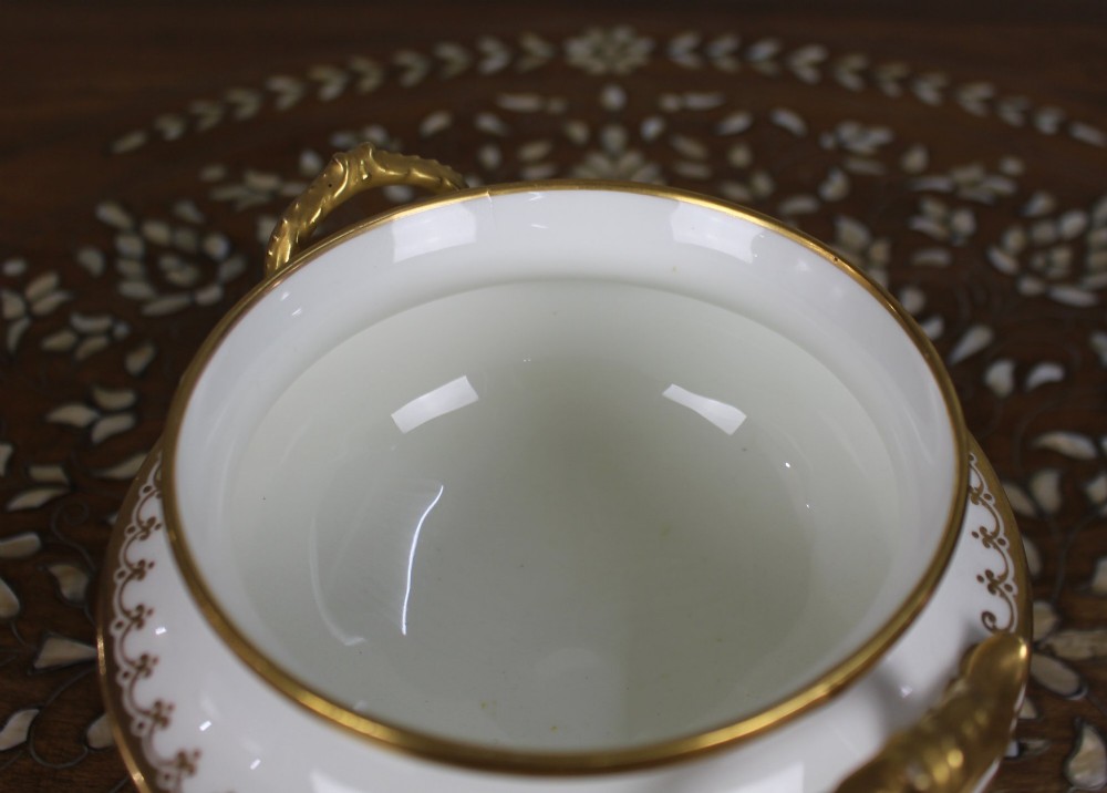 A 19th-century white porcelain urn featuring gilded side handles, a classical scroll frieze, and a fluted pedestal foot. View V