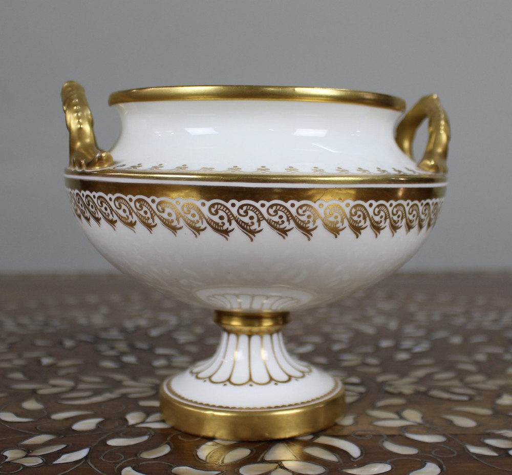 A 19th-century white porcelain urn featuring gilded side handles, a classical scroll frieze, and a fluted pedestal foot. View VII