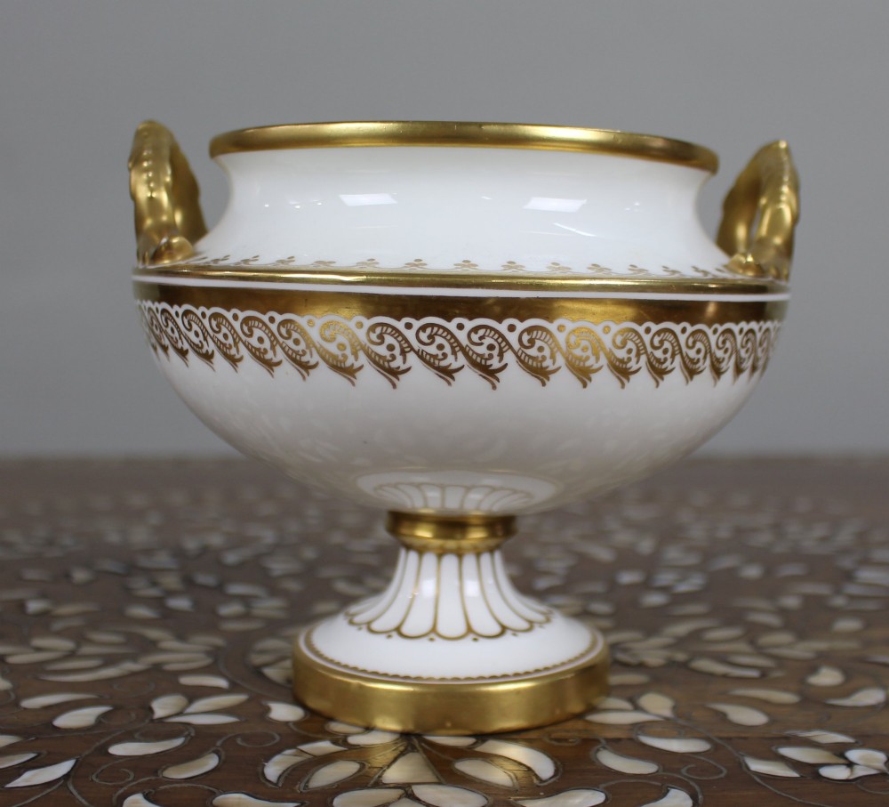 A 19th-century white porcelain urn featuring gilded side handles, a classical scroll frieze, and a fluted pedestal foot. View X