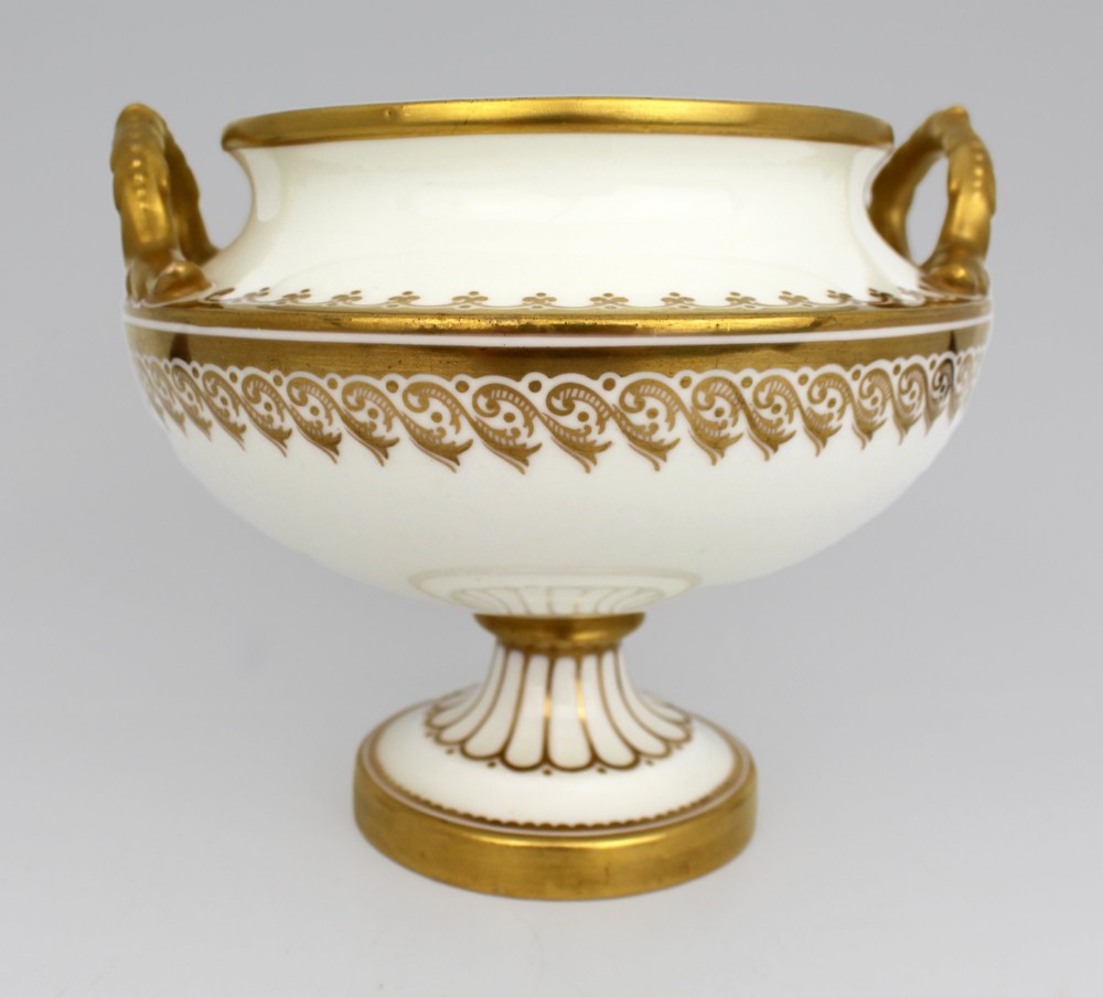 A 19th-century white porcelain urn featuring gilded side handles, a classical scroll frieze, and a fluted pedestal foot. View XI
