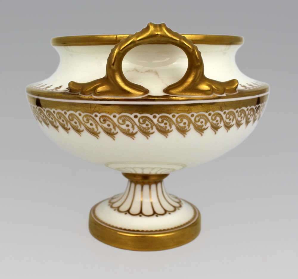 A 19th-century white porcelain urn featuring gilded side handles, a classical scroll frieze, and a fluted pedestal foot. View XIII