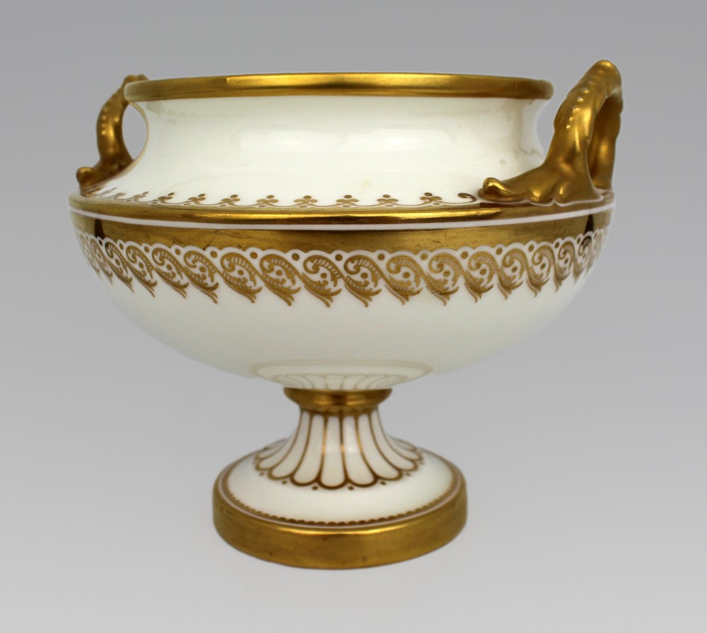 A 19th-century white porcelain urn featuring gilded side handles, a classical scroll frieze, and a fluted pedestal foot. View XIV