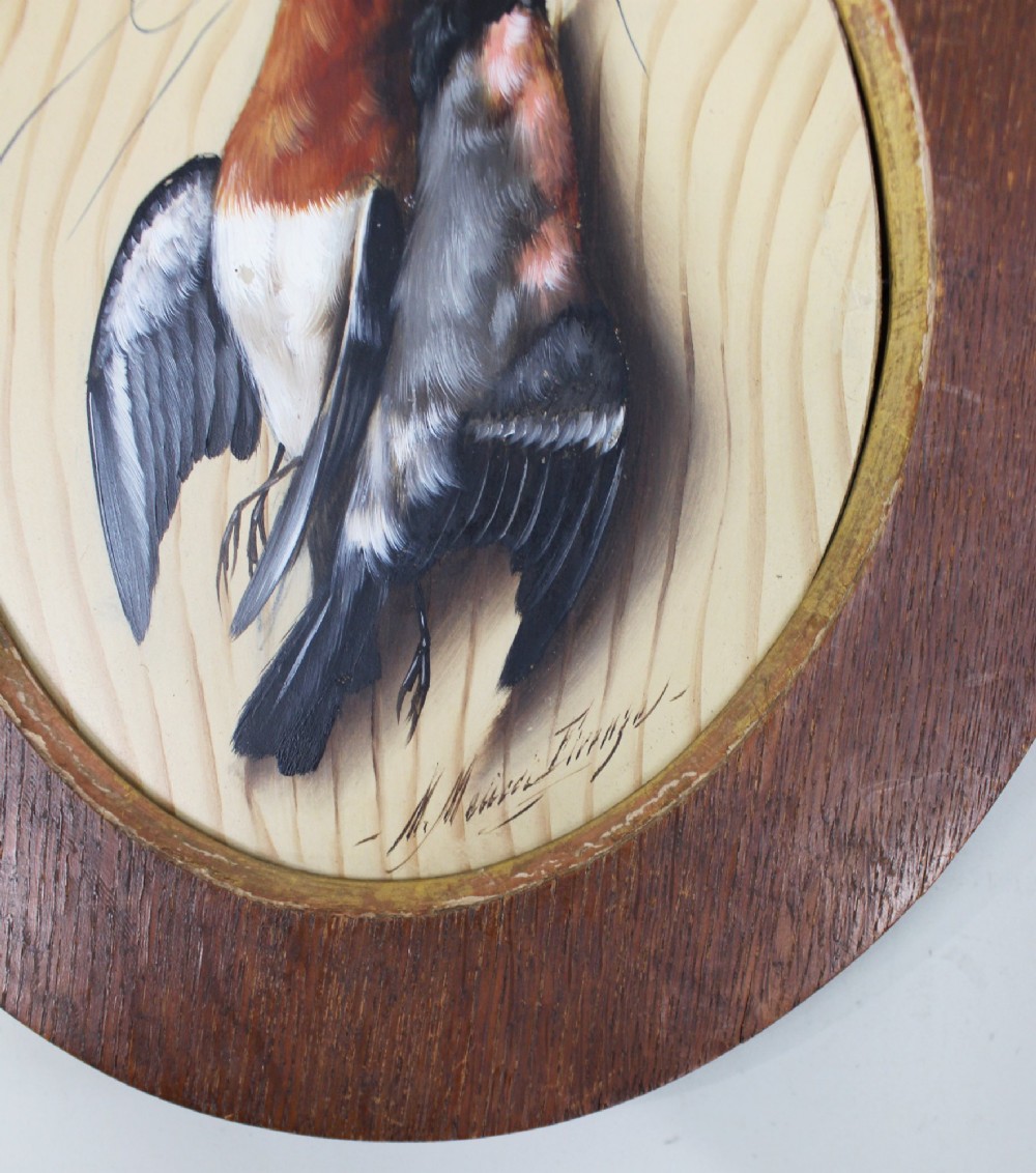 An oval oil painting on a wood panel depicting two hanging songbirds painted in trompe loeil style inside a wide wooden frame. View IV