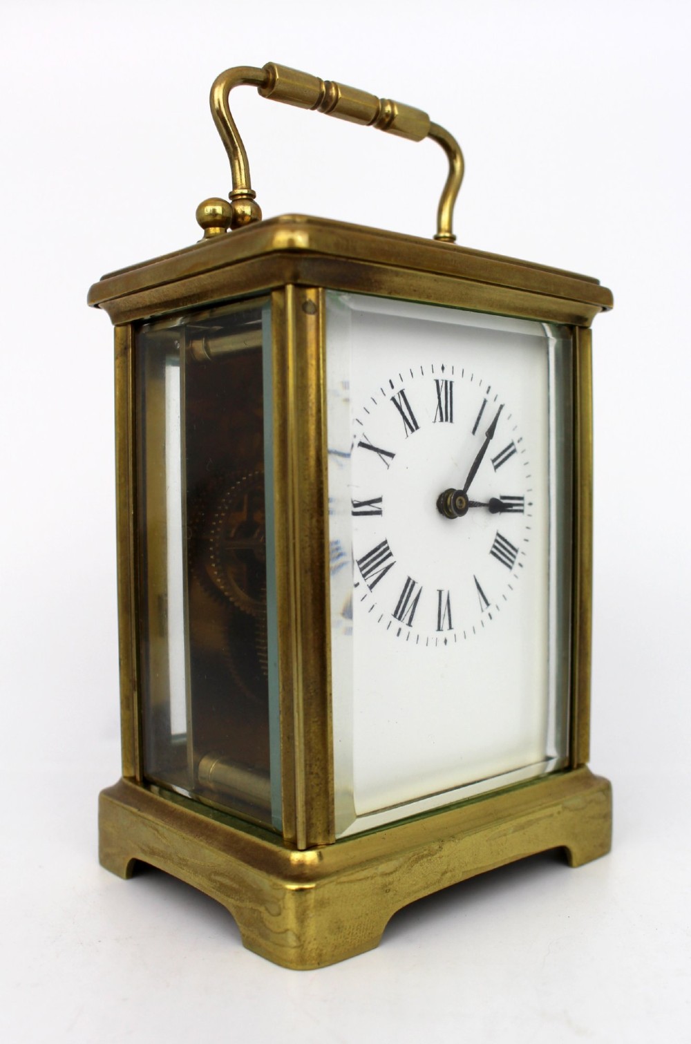 An antique brass carriage clock featuring rectangular glass side panels, a white enamel dial with black Roman numerals, and a folding top handle. View II