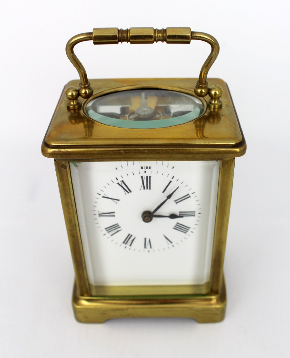 An antique brass carriage clock featuring rectangular glass side panels, a white enamel dial with black Roman numerals, and a folding top handle. View VI