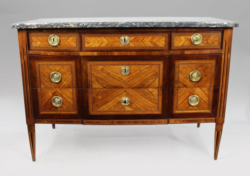 An 18th-century French Louis XVI commode featuring geometric parquetry wood inlay, tapered legs, brass ring handles, and a grey marble top.