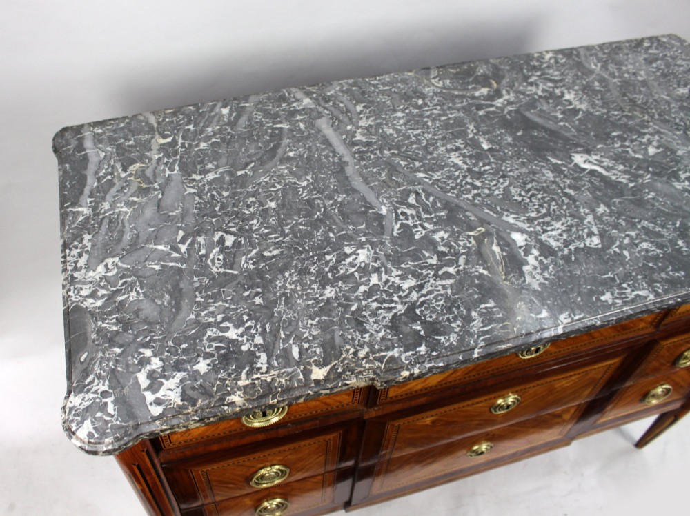 An 18th-century French Louis XVI commode featuring geometric parquetry wood inlay, tapered legs, brass ring handles, and a grey marble top. View IV