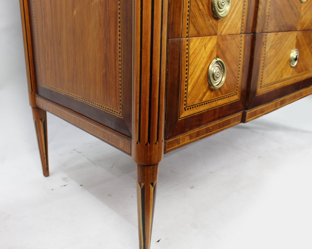 An 18th-century French Louis XVI commode featuring geometric parquetry wood inlay, tapered legs, brass ring handles, and a grey marble top. View IX
