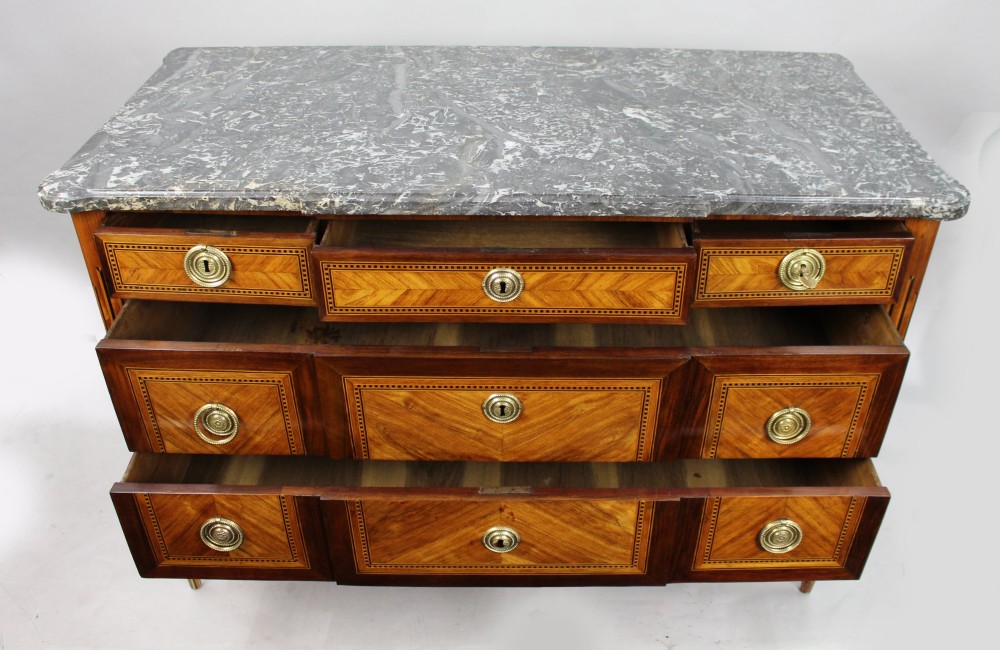 An 18th-century French Louis XVI commode featuring geometric parquetry wood inlay, tapered legs, brass ring handles, and a grey marble top. View X