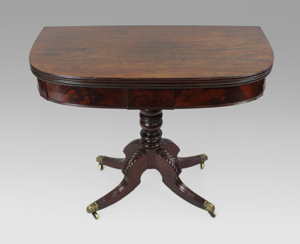 An early nineteenth-century Regency mahogany tea table with a folded rounded top resting on a turned central column and four splayed legs with brass castors.
