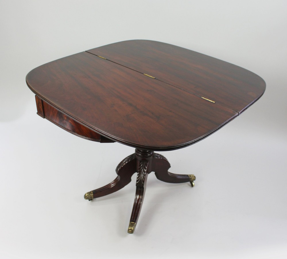 An early nineteenth-century Regency mahogany tea table with a folded rounded top resting on a turned central column and four splayed legs with brass castors. View VI