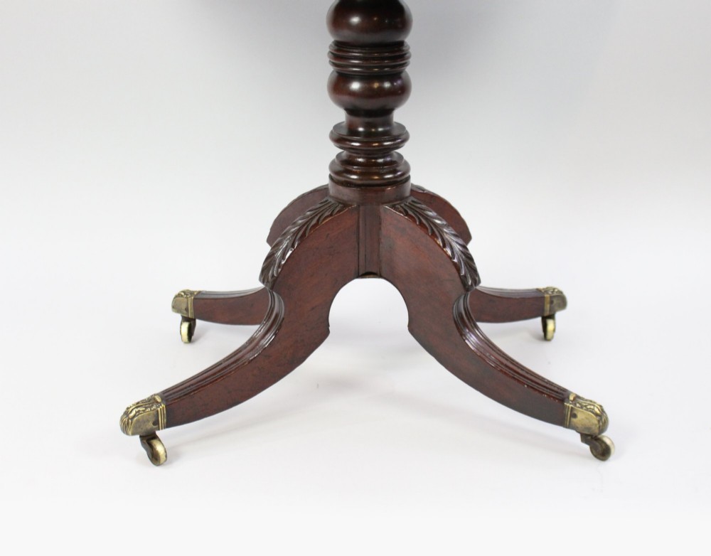 An early nineteenth-century Regency mahogany tea table with a folded rounded top resting on a turned central column and four splayed legs with brass castors. View X