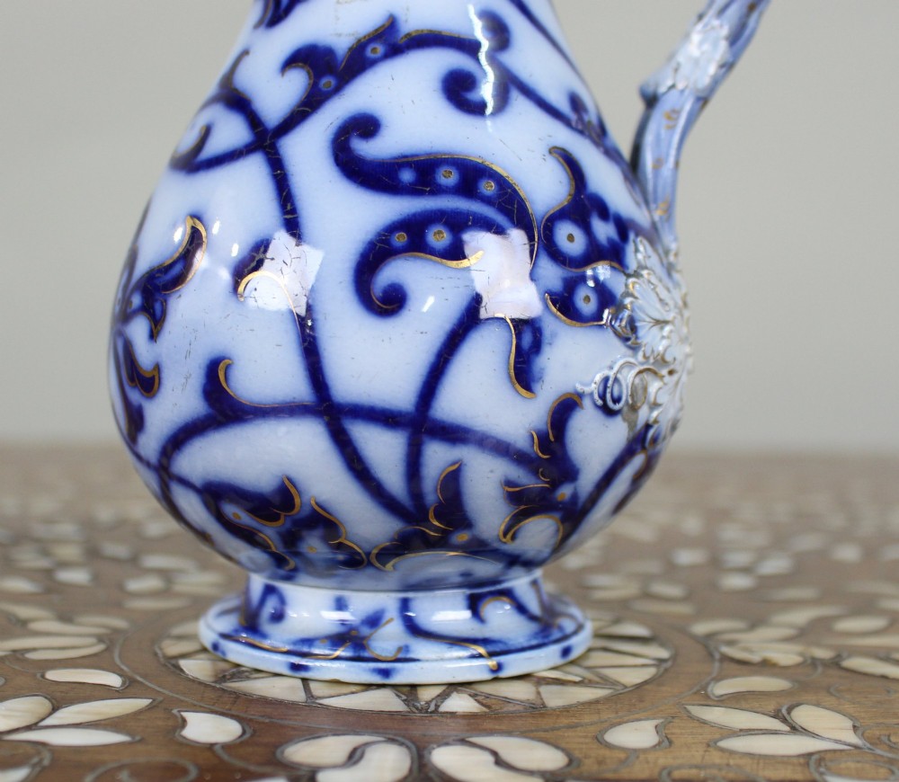 A Victorian relief-moulded flow blue earthenware jug decorated with cobalt scrollwork, white floral details with gold accents, and a hinged pewter lid. View III