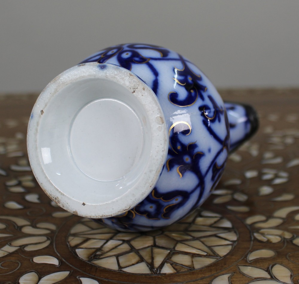 A Victorian relief-moulded flow blue earthenware jug decorated with cobalt scrollwork, white floral details with gold accents, and a hinged pewter lid. View VII