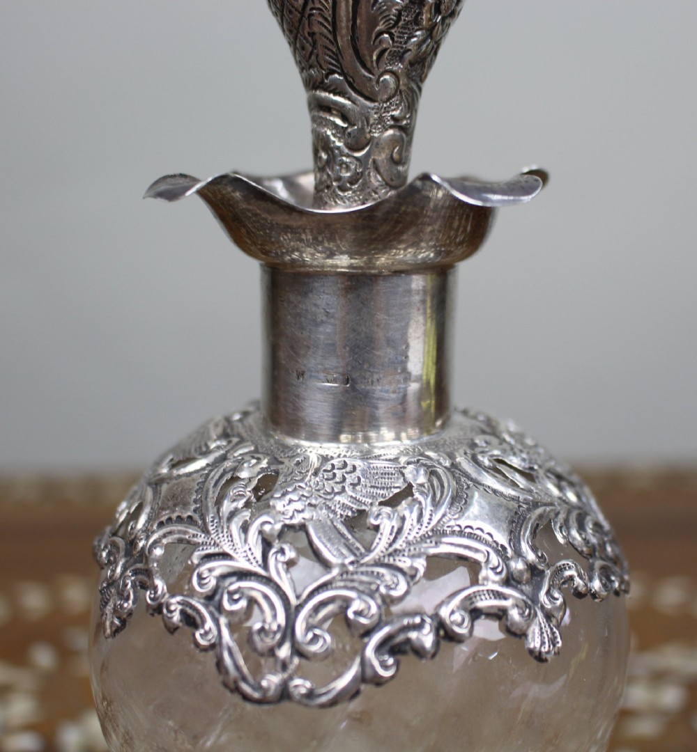 An antique clear glass decanter featuring a pinched waist, swirled body, ornate pierced silver shoulder mount, silver collar, and a chased silver stopper. View III