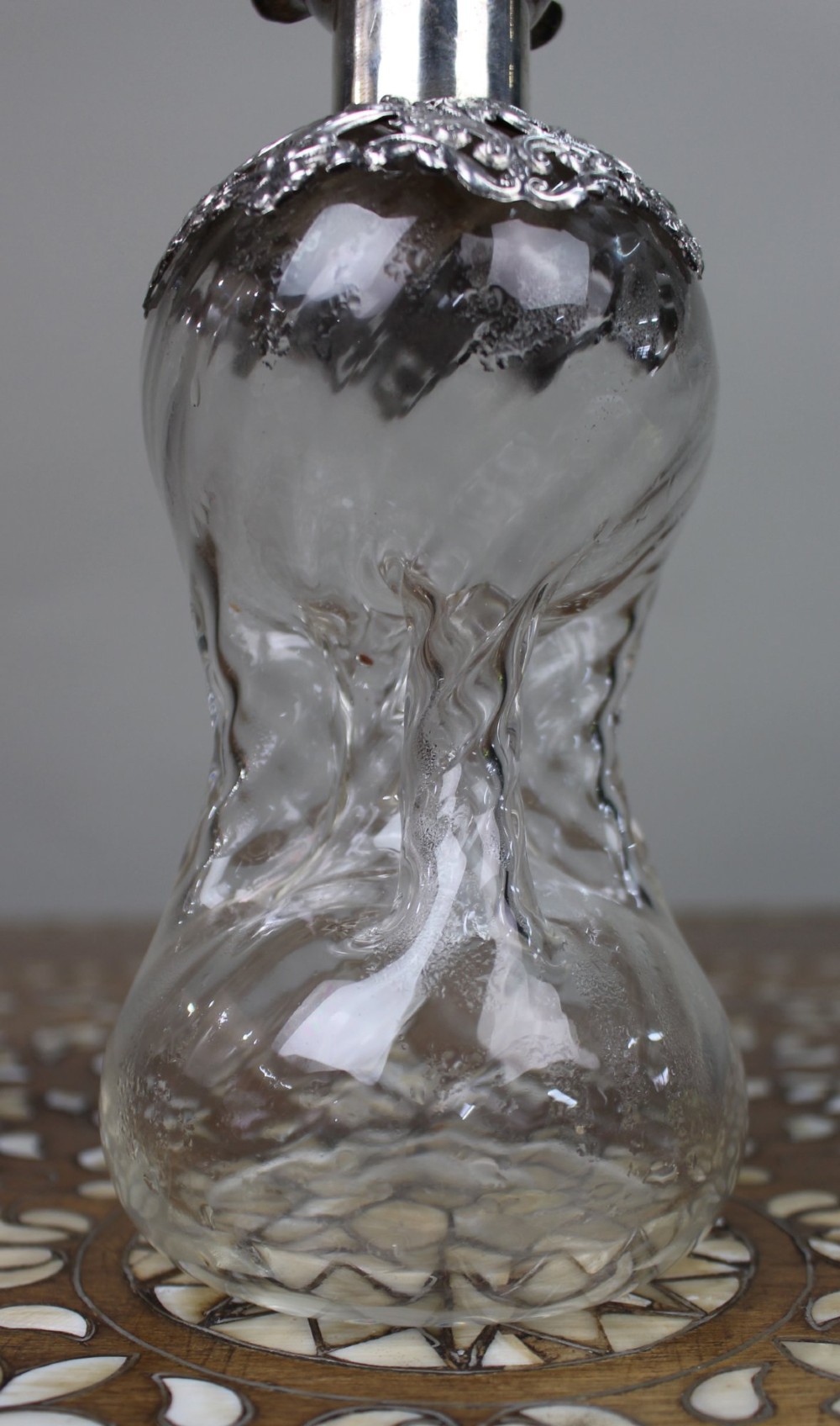 An antique clear glass decanter featuring a pinched waist, swirled body, ornate pierced silver shoulder mount, silver collar, and a chased silver stopper. View IV
