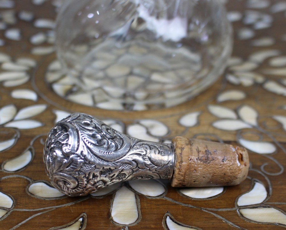 An antique clear glass decanter featuring a pinched waist, swirled body, ornate pierced silver shoulder mount, silver collar, and a chased silver stopper. View VII