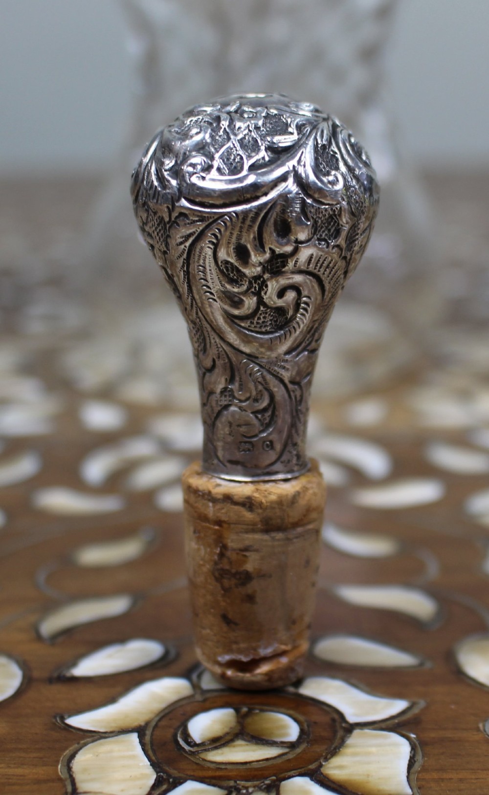 An antique clear glass decanter featuring a pinched waist, swirled body, ornate pierced silver shoulder mount, silver collar, and a chased silver stopper. View VIII