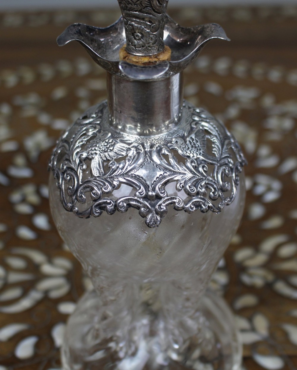 An antique clear glass decanter featuring a pinched waist, swirled body, ornate pierced silver shoulder mount, silver collar, and a chased silver stopper. View XI