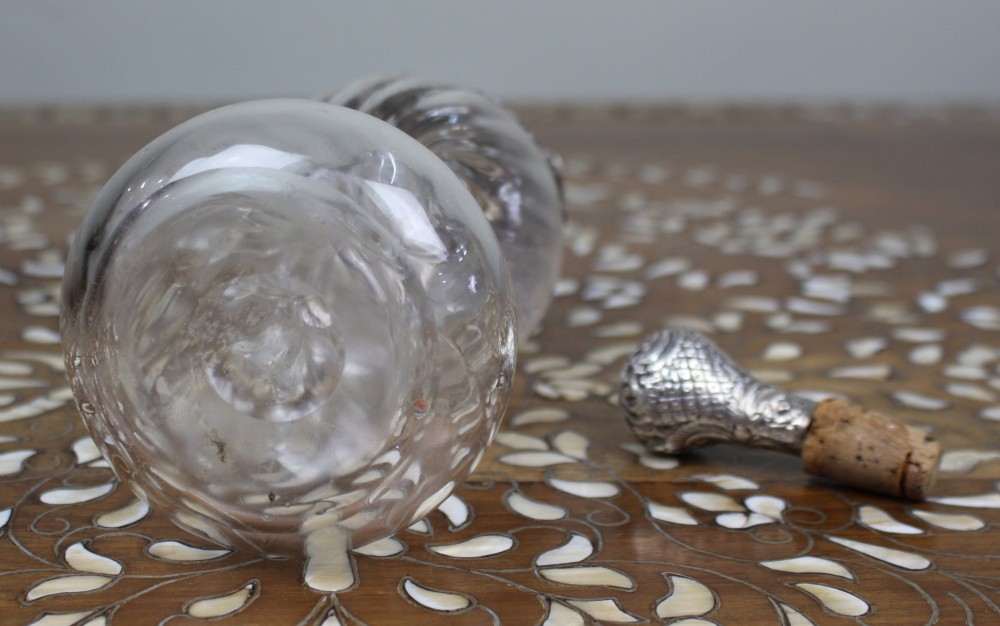 An antique clear glass decanter featuring a pinched waist, swirled body, ornate pierced silver shoulder mount, silver collar, and a chased silver stopper. View XII