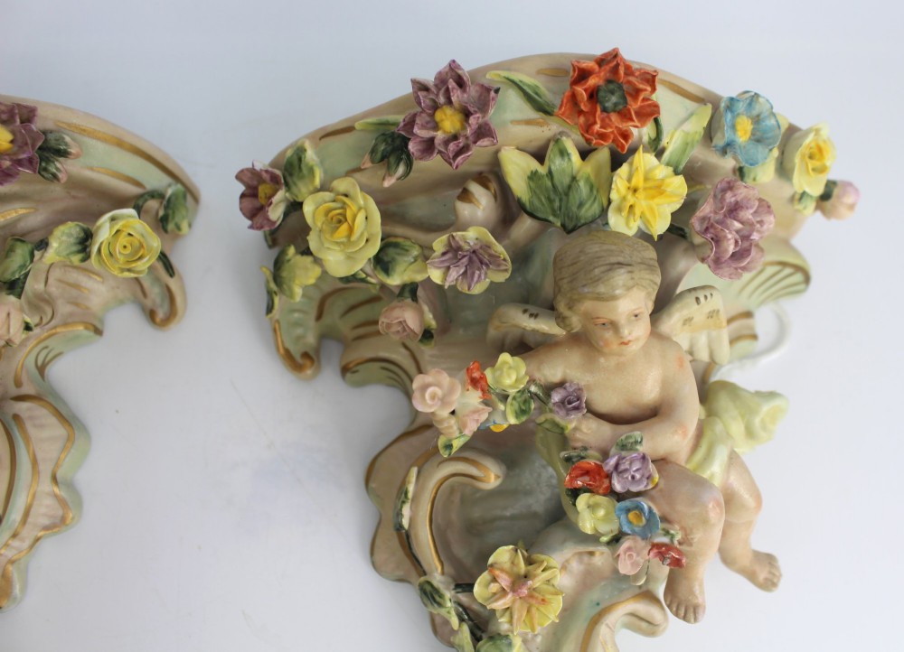 A pair of Rococo Revival porcelain wall corbels decorated with sculpted cherubs, elaborate scrollwork, and colourful encrusted flowers with gilt accents. View V