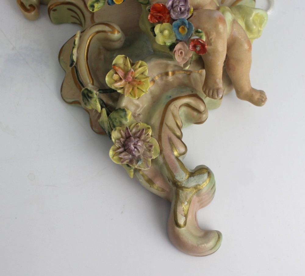 A pair of Rococo Revival porcelain wall corbels decorated with sculpted cherubs, elaborate scrollwork, and colourful encrusted flowers with gilt accents. View VI