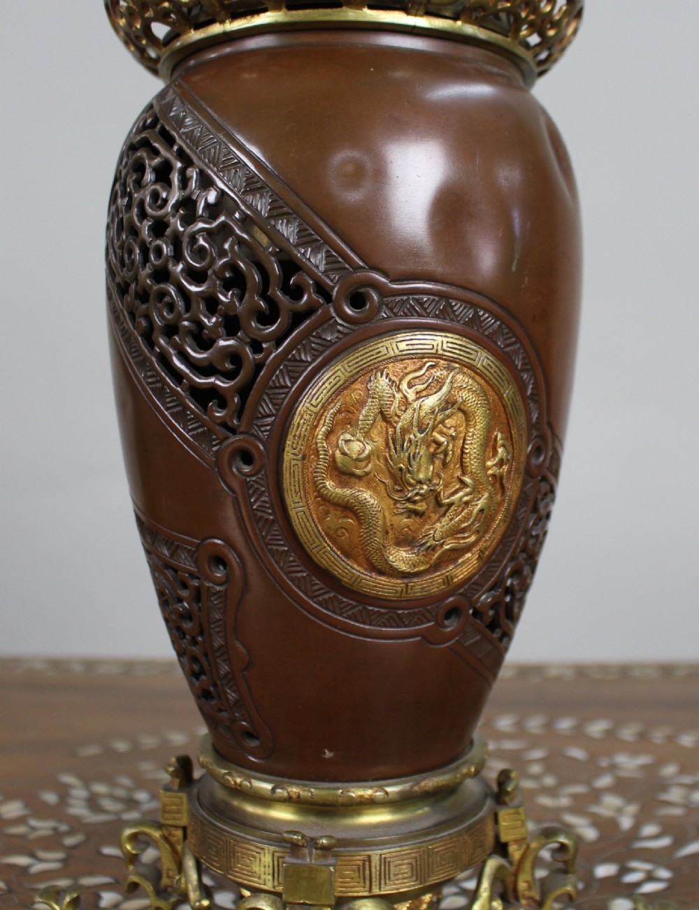 A Meiji period Japanese dark brown bronze oil lamp featuring reticulated openwork, a gilded dragon roundel, brass burner fittings, and decorative scroll feet. View III