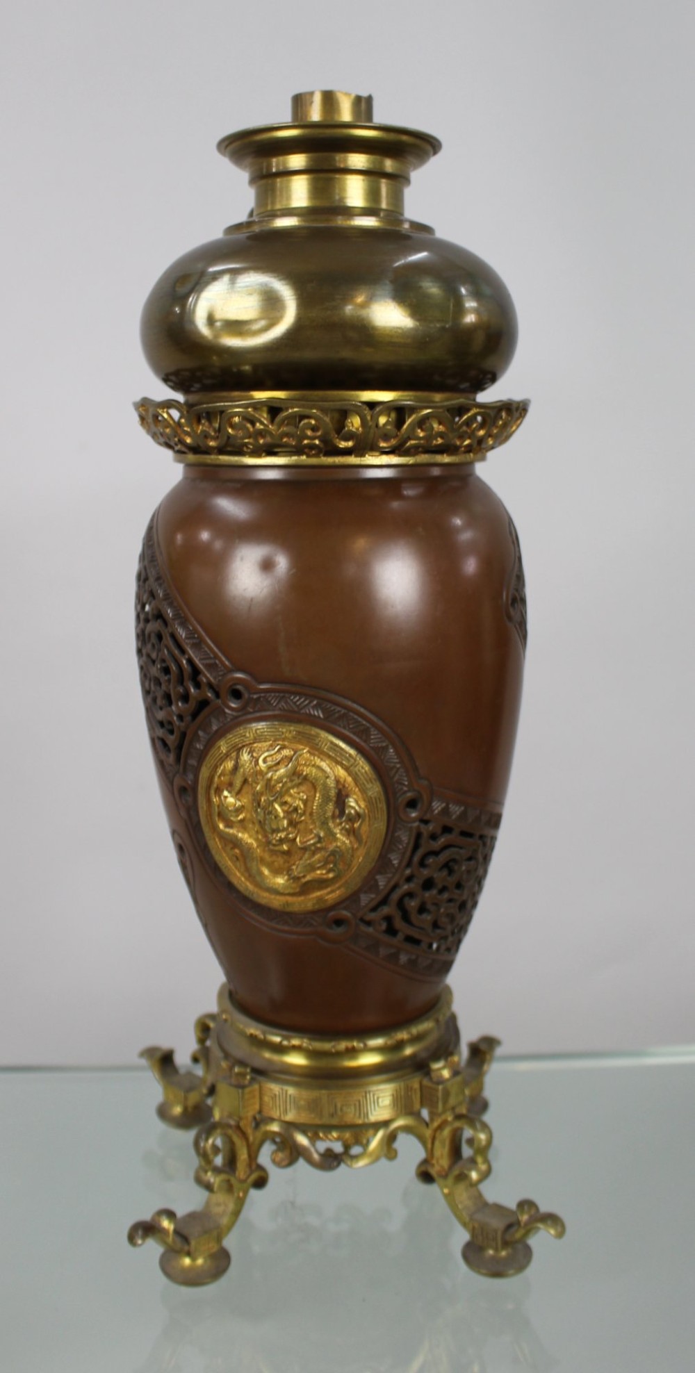 A Meiji period Japanese dark brown bronze oil lamp featuring reticulated openwork, a gilded dragon roundel, brass burner fittings, and decorative scroll feet. View VI