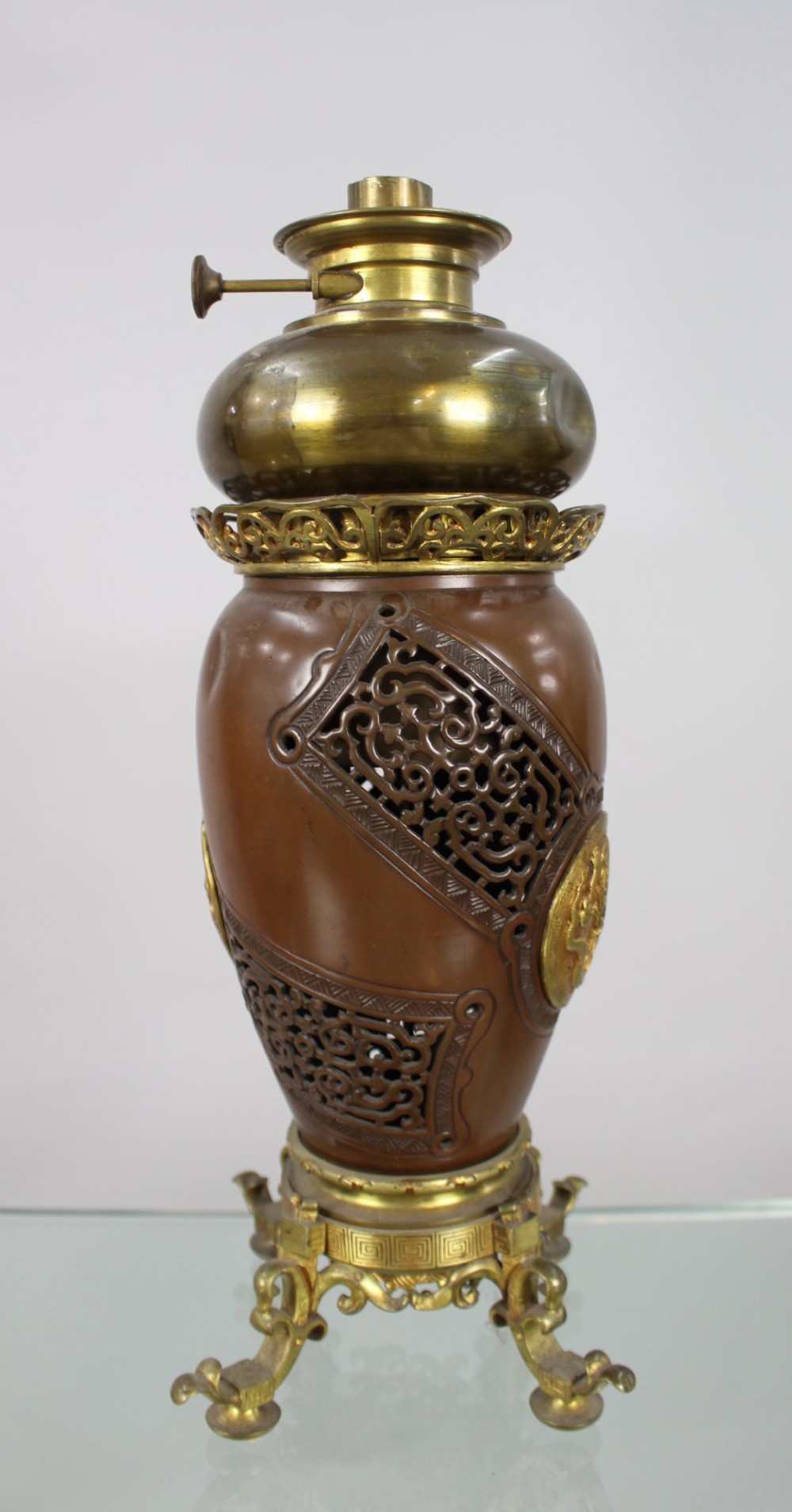 A Meiji period Japanese dark brown bronze oil lamp featuring reticulated openwork, a gilded dragon roundel, brass burner fittings, and decorative scroll feet. View VII