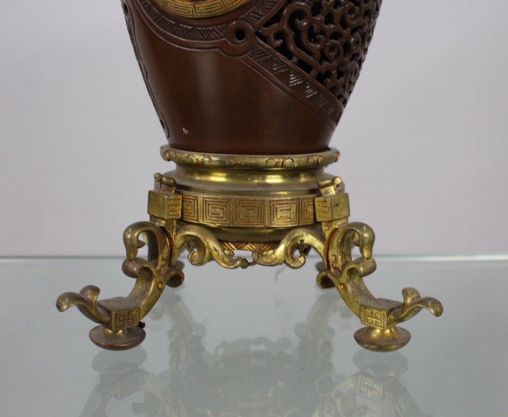 A Meiji period Japanese dark brown bronze oil lamp featuring reticulated openwork, a gilded dragon roundel, brass burner fittings, and decorative scroll feet. View IX