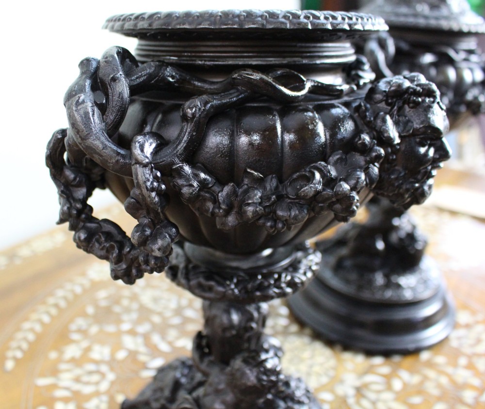 A pair of dark bronzed spelter urns with lids topped by seated putti figures, featuring Bacchic masks, relief garlands, and bases supported by sculpted cherubs. View XIII