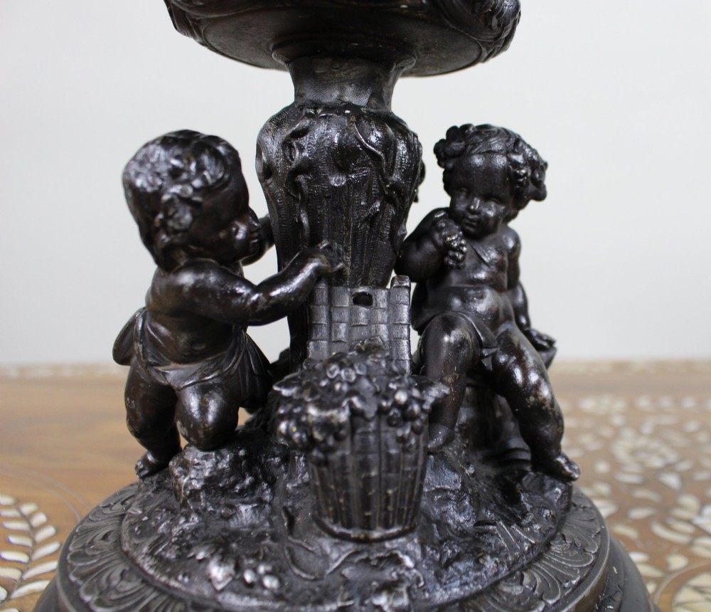 A pair of dark bronzed spelter urns with lids topped by seated putti figures, featuring Bacchic masks, relief garlands, and bases supported by sculpted cherubs. View XIV