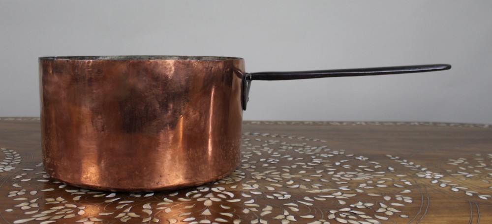 A large antique Georgian copper saucepan featuring a straight cylindrical body and a long wrought iron handle fastened with metal rivets.