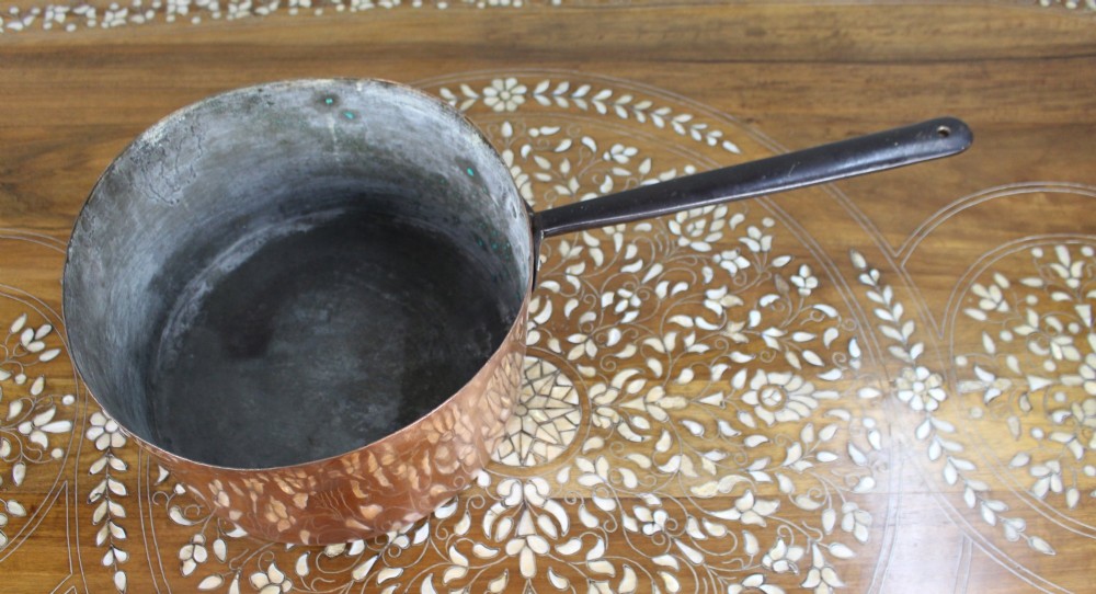 A large antique Georgian copper saucepan featuring a straight cylindrical body and a long wrought iron handle fastened with metal rivets. View V