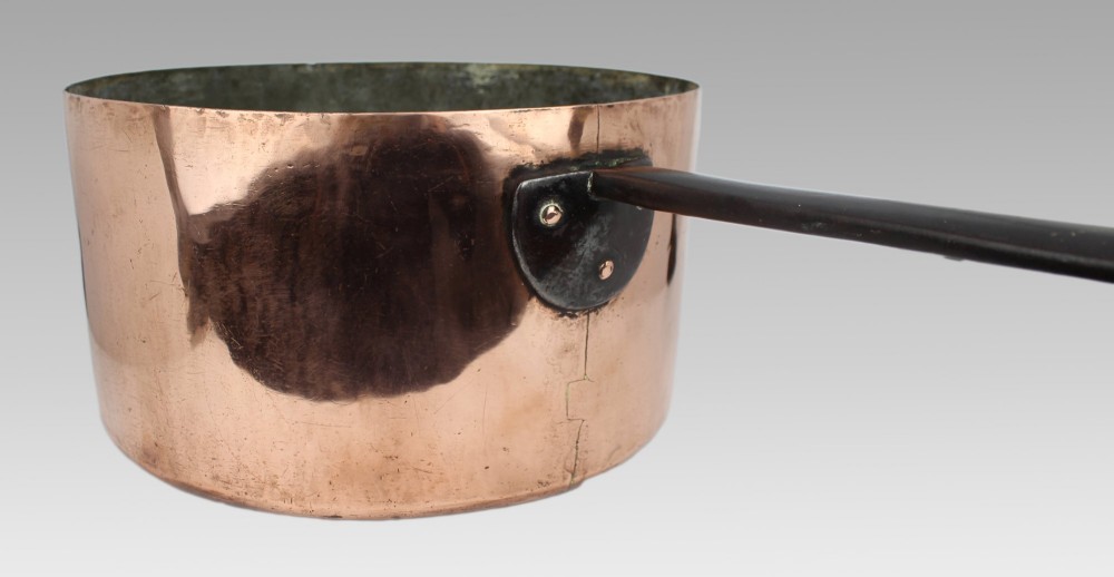 A large antique Georgian copper saucepan featuring a straight cylindrical body and a long wrought iron handle fastened with metal rivets. View VIII