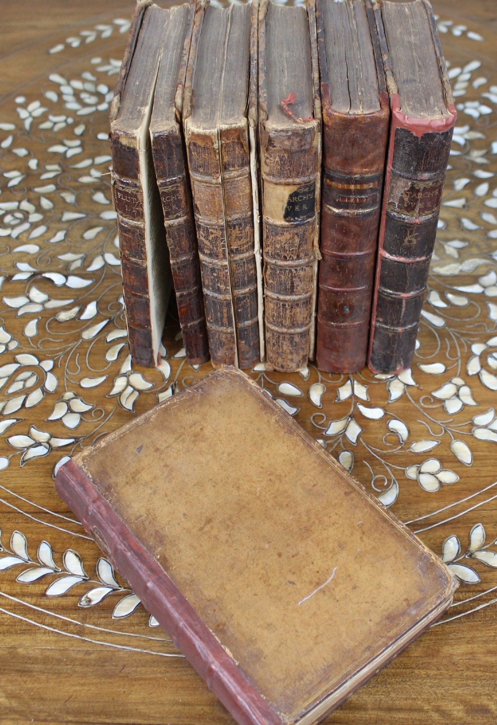 A six-volume set of eighteenth-century leather-bound books with distressed brown spines and gilt lettering standing upright. View VI