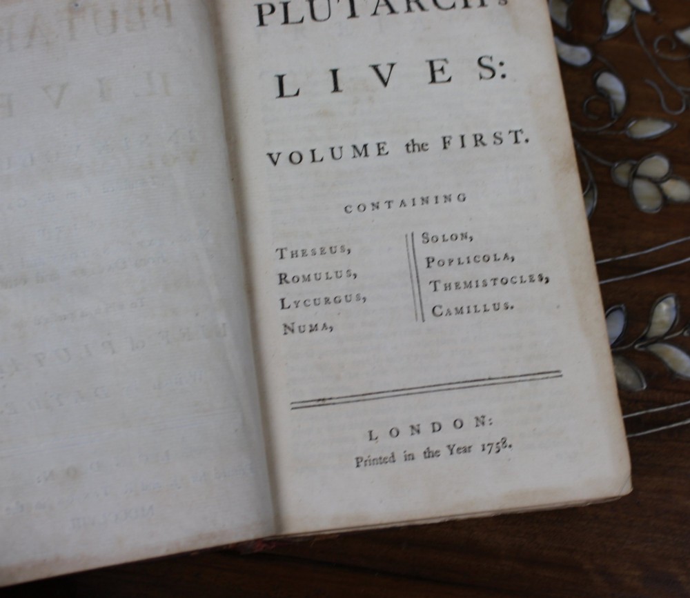 A six-volume set of eighteenth-century leather-bound books with distressed brown spines and gilt lettering standing upright. View X